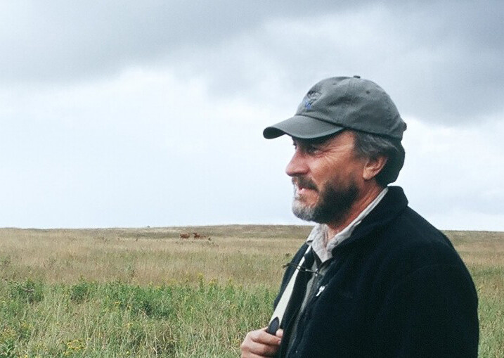 Lorne Fitch standing in a field speaking with someone while cows graze in the background.