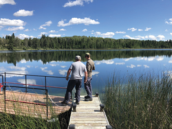 Two men stand on a dock looking out at Gerharts Lake on a summer day.