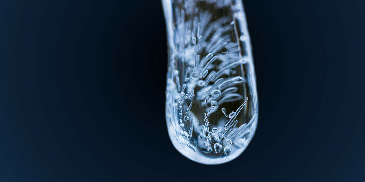 Frozen drop of water dangling in front of a dark background.