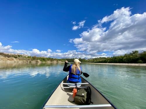 Woman paddling in canoe with clear water and blue skies.